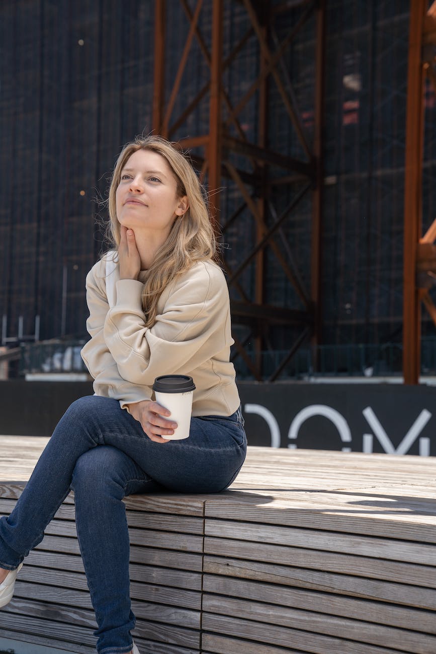 woman sitting on a wooden bench holding a cup of coffee